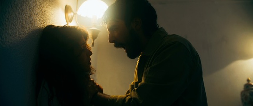Duas personagens frente a frente num corredor iluminado por luz quente.